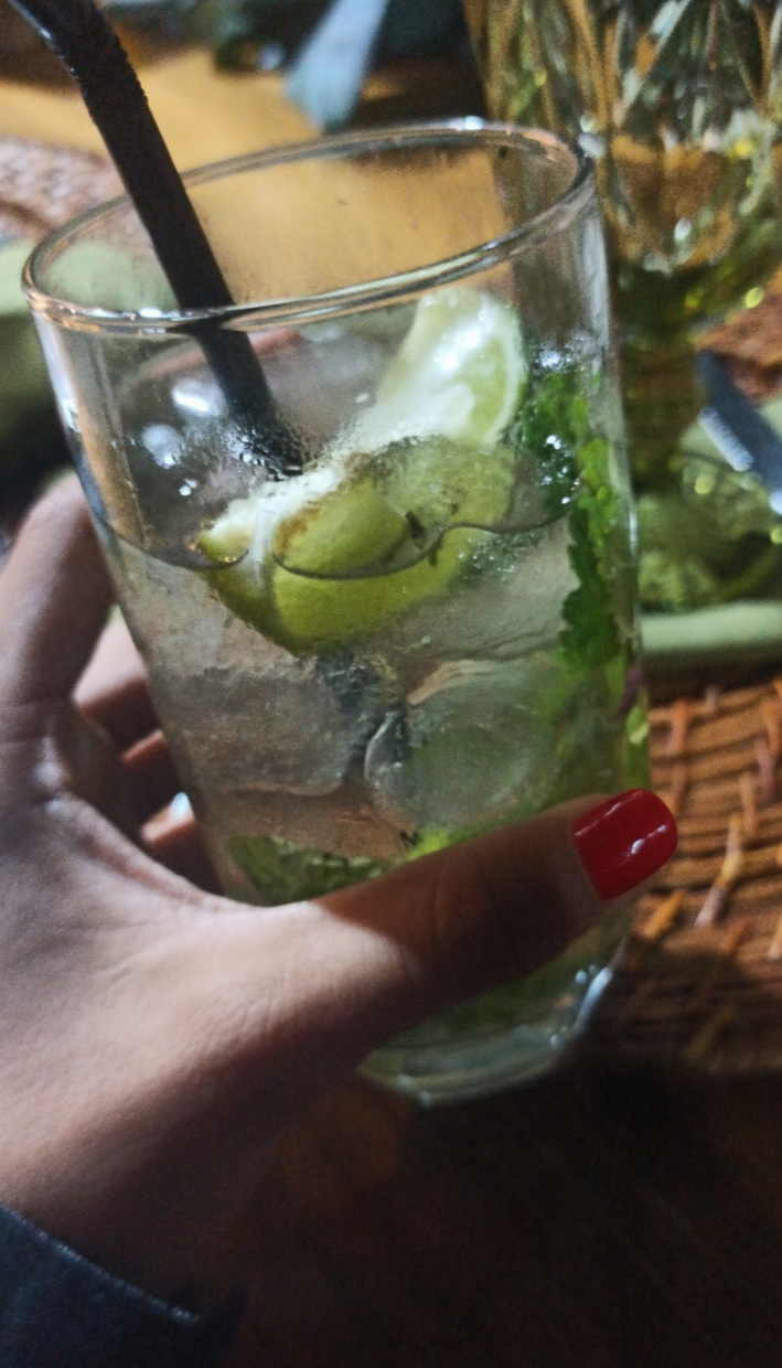 Hand holding a glass of iced drink with lime and mint leaves on a wooden table.
